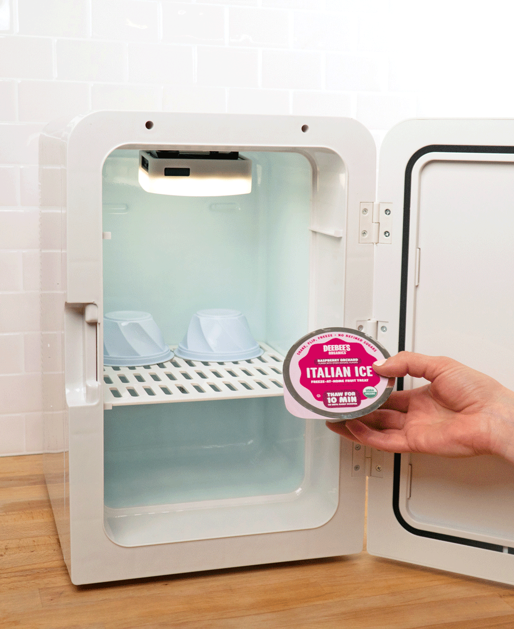 A hand flips a DeeBee's Organics Italian Ice cup upside down while putting it into a small white freezer. 
