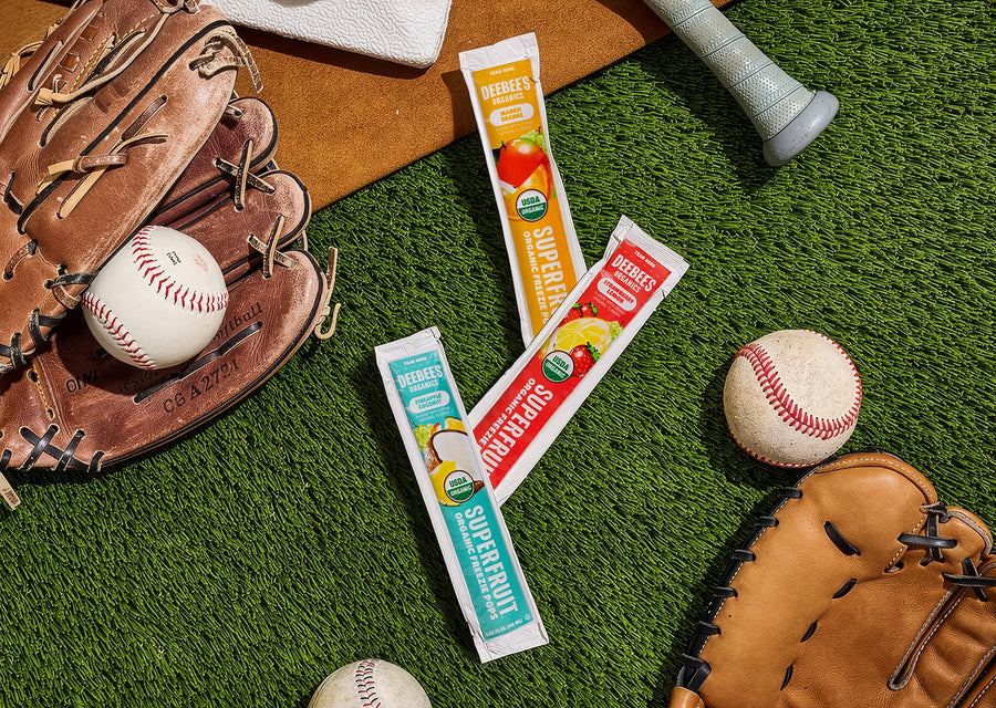 DeeBee’s Organics SuperFruit Freezies in mango orange, strawberry lemonade, and pineapple coconut flavors on grass with baseball glove and balls