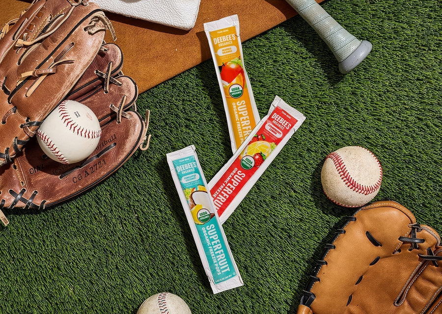 DeeBee’s Organics SuperFruit Freezies in mango orange, strawberry lemonade, and pineapple coconut flavors on grass with baseball glove and balls