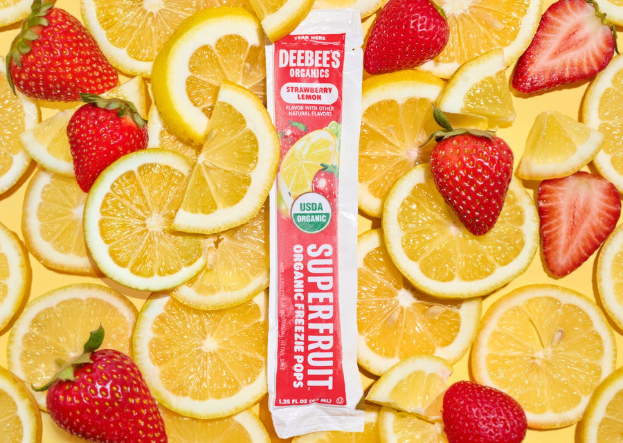 DeeBee’s Organics Strawberry Lemon SuperFruit Freezie surrounded by fresh lemon slices and whole strawberries on a bright yellow background