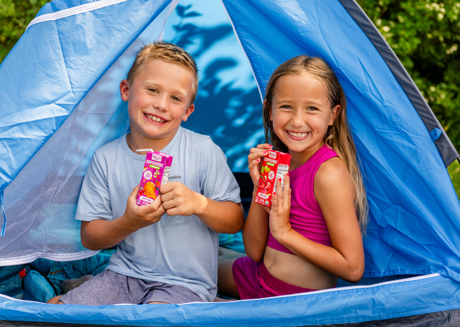 Kids enjoying a summer camping adventure in a backyard tent while drinking DeeBee's Organics SuperFruit Prebiotic Juice Boxes, creating fun family summer memories.