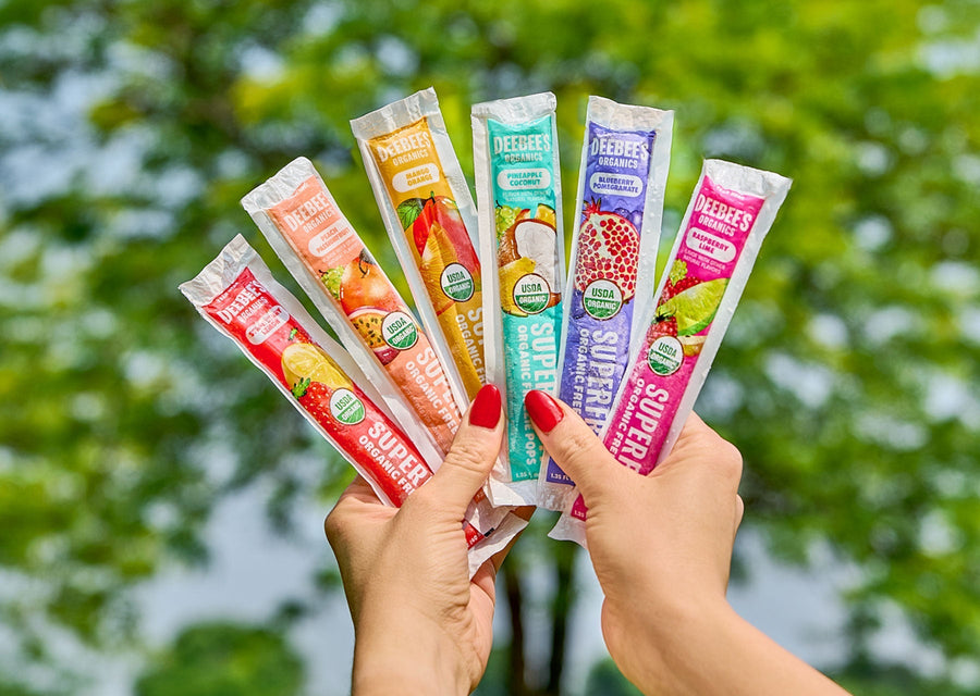Hands holding a fan of colorful DeeBee’s Organics SuperFruit freezie pops outdoors.