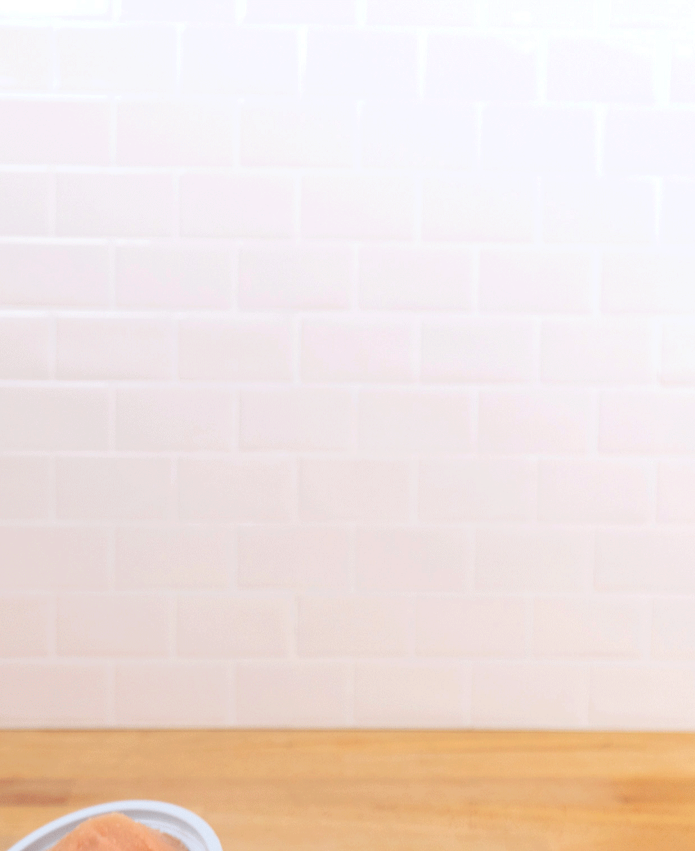 A hand holds up an open DeeBee's Organics Italian Ice cup against a white tile background. 