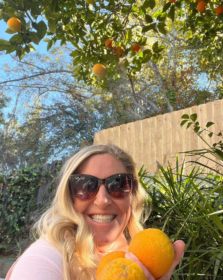 Dr. Dionne Laslo-Baker holding fresh oranges under an orange tree